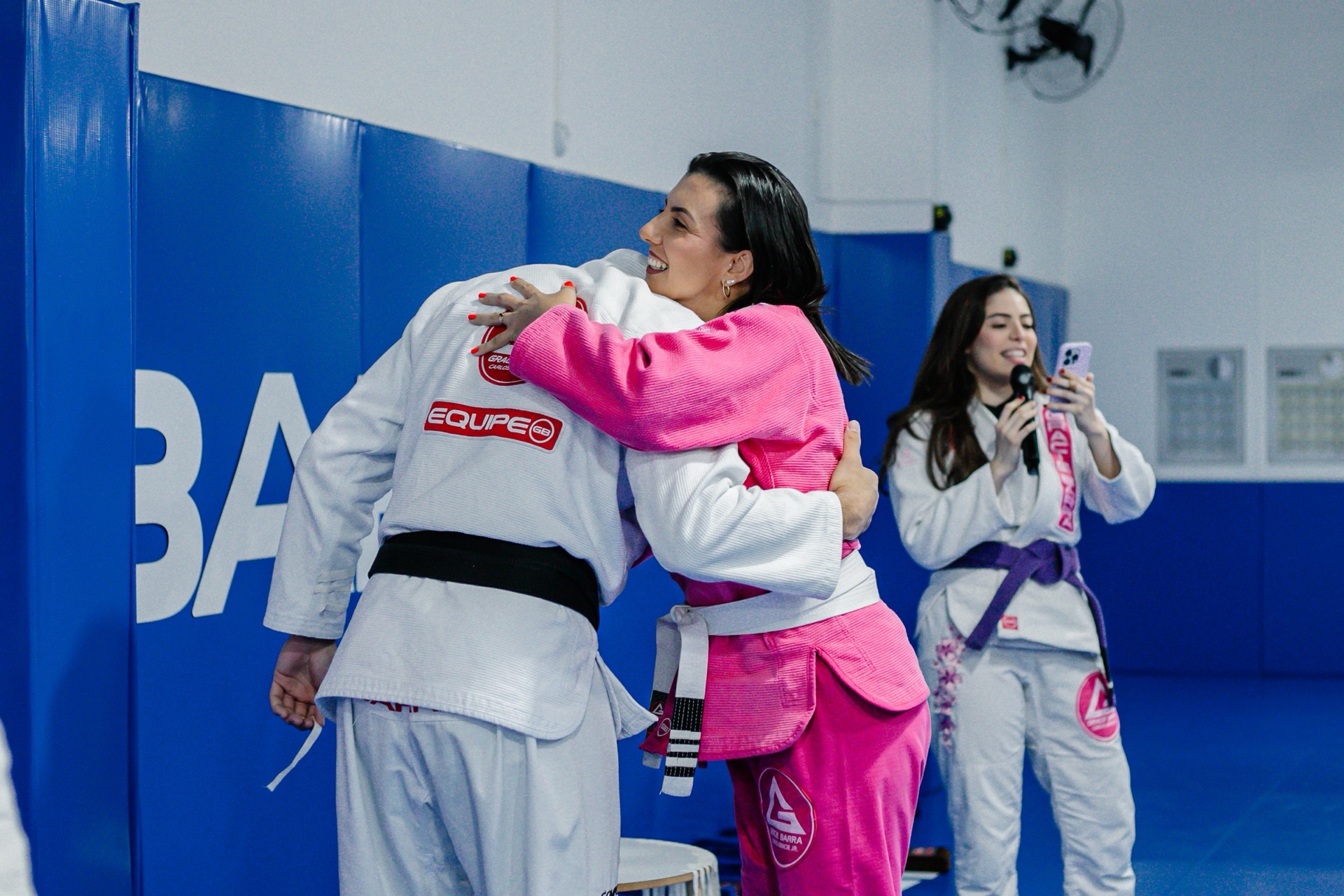 Duas alunas se abraçando no tatame, uma de kimono rosa