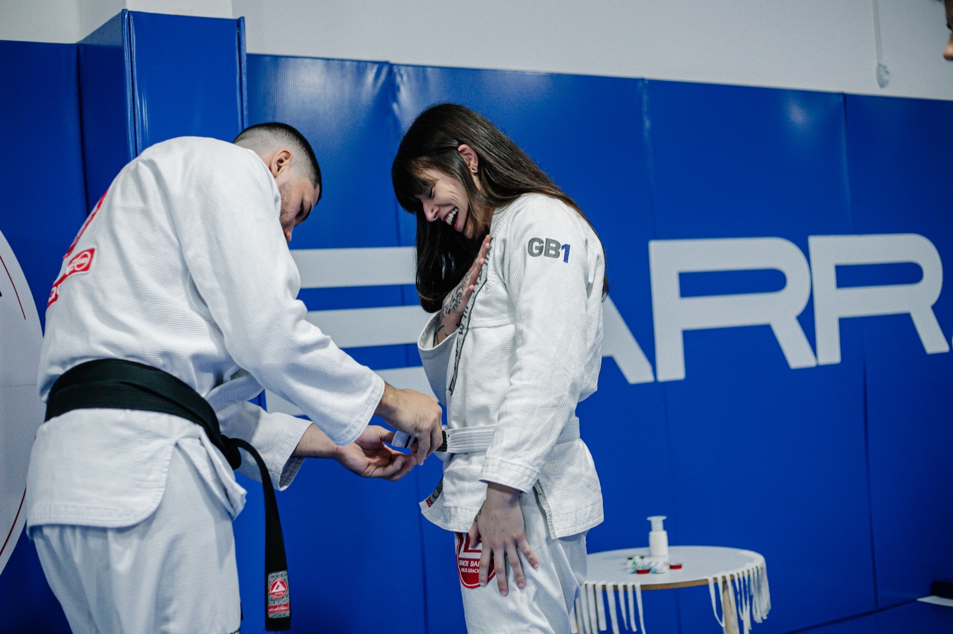 Instrutor faixa preta amarrando a nova faixa de uma aluna durante a cerimônia de graduação da Gracie Barra Tubarão