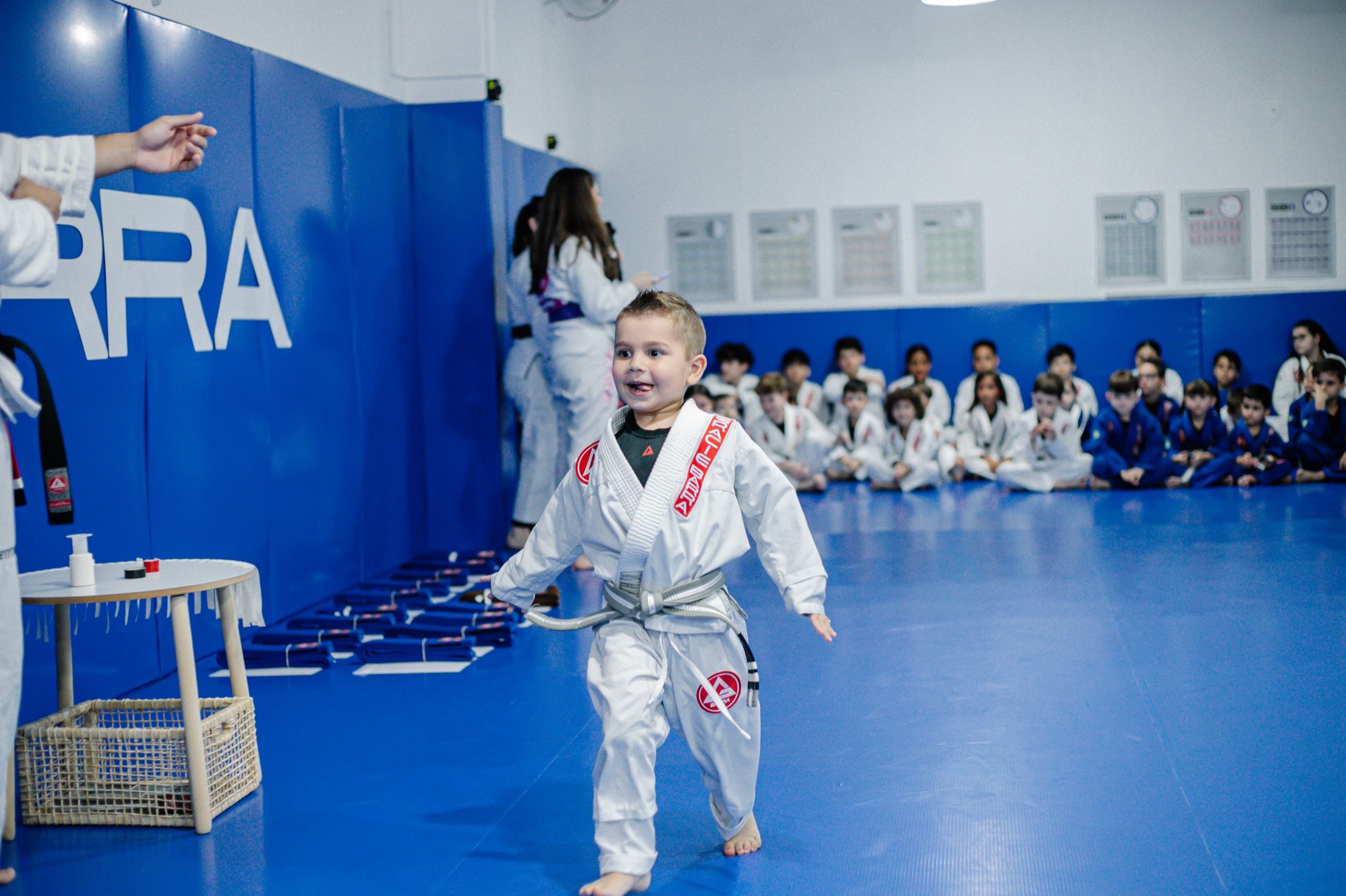 Tatame azul da Gracie Barra Tubarão com um aluno Kids em pé e a turma sentada ao fundo