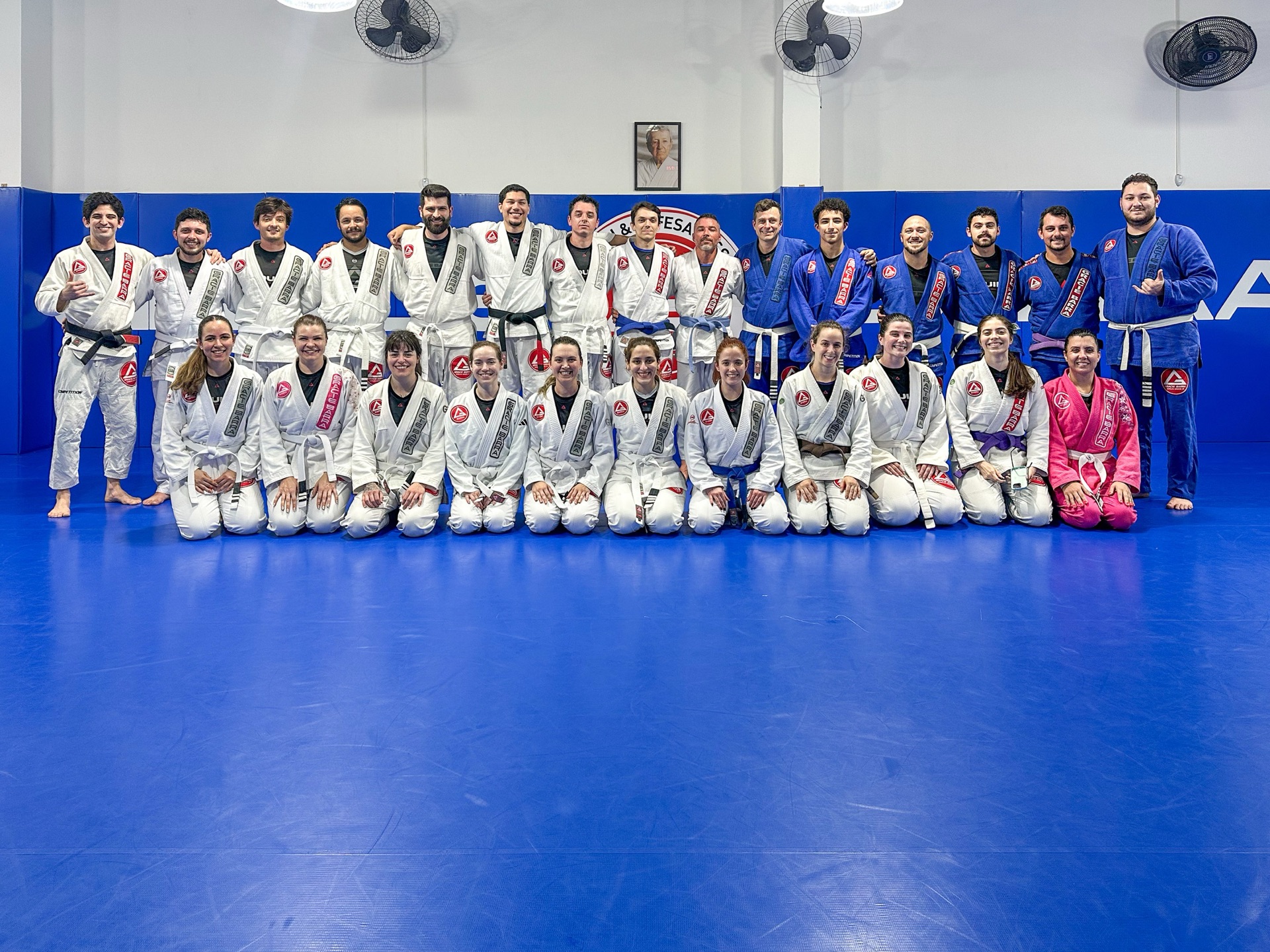 Turma da Gracie Barra Tubarão com instrutores reunida no tatame azul diante do escudo