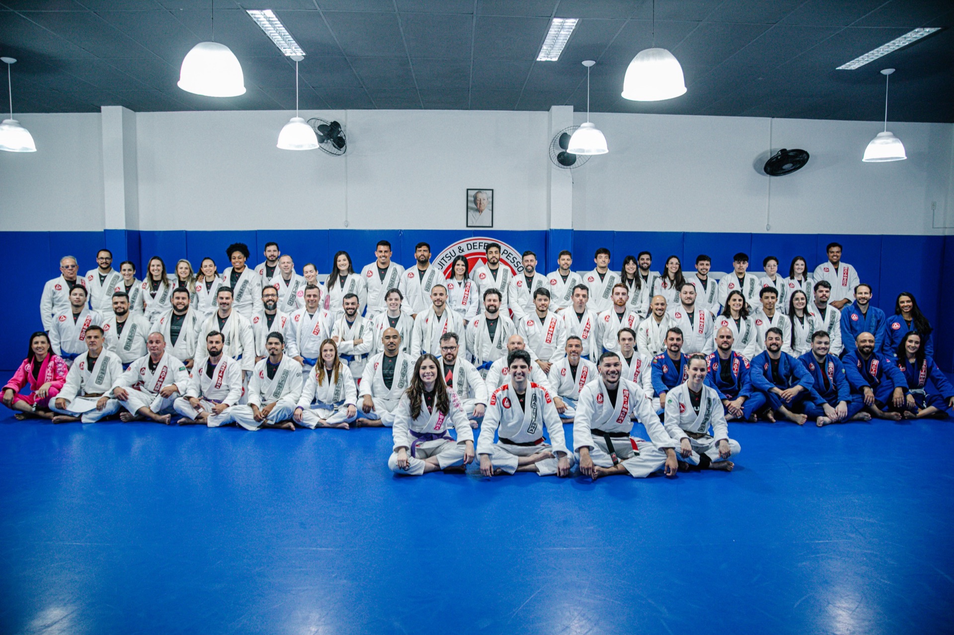 Turma completa da Gracie Barra Tubarão reunida no tatame azul, alunos e instrutores de várias idades e faixas
